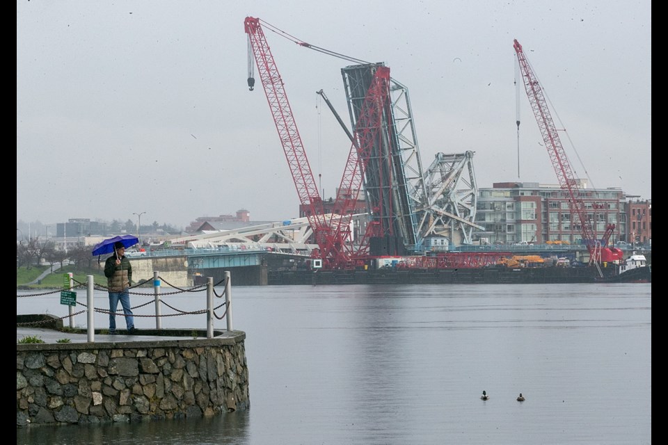 John Peters walks in the rain in front of the Laurel Point as the construction continues on the new bridge in the background.