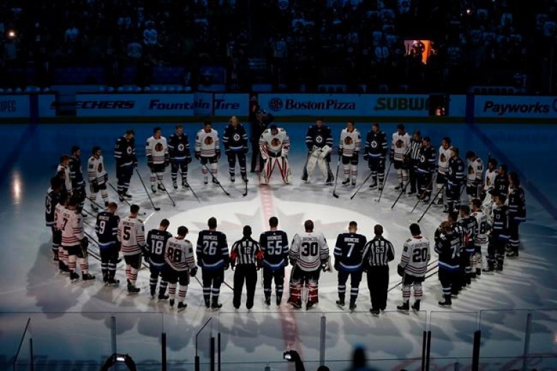 Winnipeg Jets and the Chicago Blackhawks come together at centre ice wearing Broncos on the back of their jerseys for a moment of silence for the Humboldt Broncos bus crash victims before NHL action in Winnipeg on Saturday, April 7, 2018.