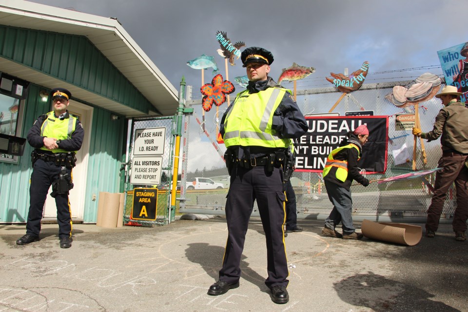 Burnaby RCMP police officers stand in front of the gates at the Trans Mountain terminal in Burnaby on Thursday, while demonstrators collect signs put up for a protest that morning.