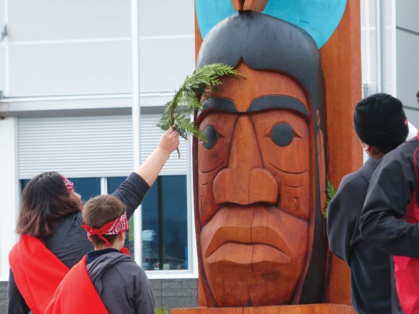 Witnesses cleanse the Chekwelhp story pole with cedar boughs drenched in water at the April 19 welcoming ceremony for the pole at Gibsons Elementary.
