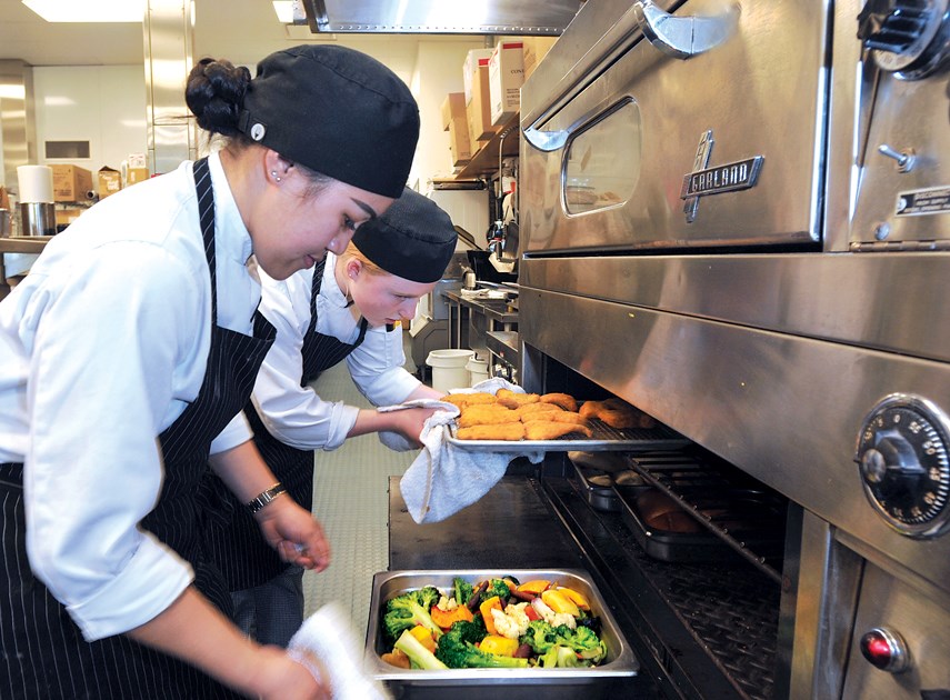 Carson Graham students Hannah Abbas and Abbey Moffat pull food dishes out of warming ovens.