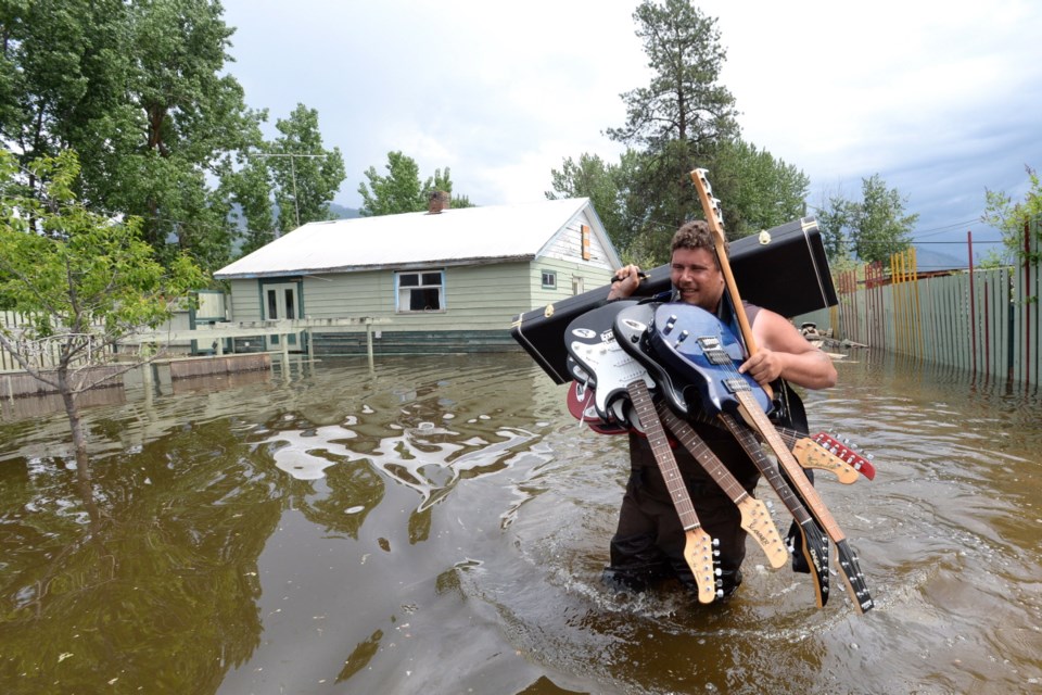 Resident Lars Androsoff carries his friend's guitars as he walks through the floodwaters in Grand Forks, B.C., on Thursday, May 17, 2018. THE CANADIAN PRESS/Jonathan Hayward