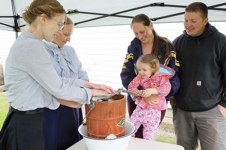 From right, Dustin Zolnai, Kat Kostukevich, and daughter Quinn, 2, try their hand at making ice cream with the help of Heritage Interpreters Danica Hoffart, and Hailey Friesen on Sunday at Huble Homestead's Spring on the Homestead event.