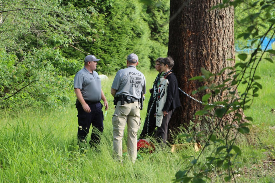 Burnaby RCMP police officers speak with two protesters chained to a tree west of the Trans Mountain terminal on Burnaby Mountain.