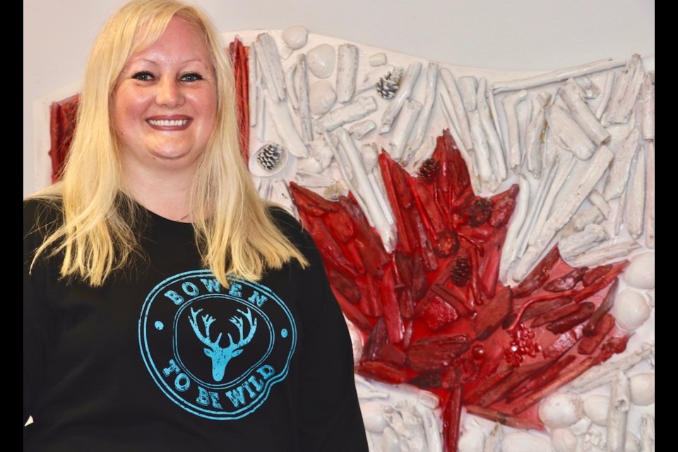 Rebecca Smith stands with the driftwood mosaic piece created for the 50th anniversary of the Canadian flag. It now hangs in municipal council chambers. Smith says she didn't have pinecones set out for the piece, so people probably picked them up from around Crippen Park.