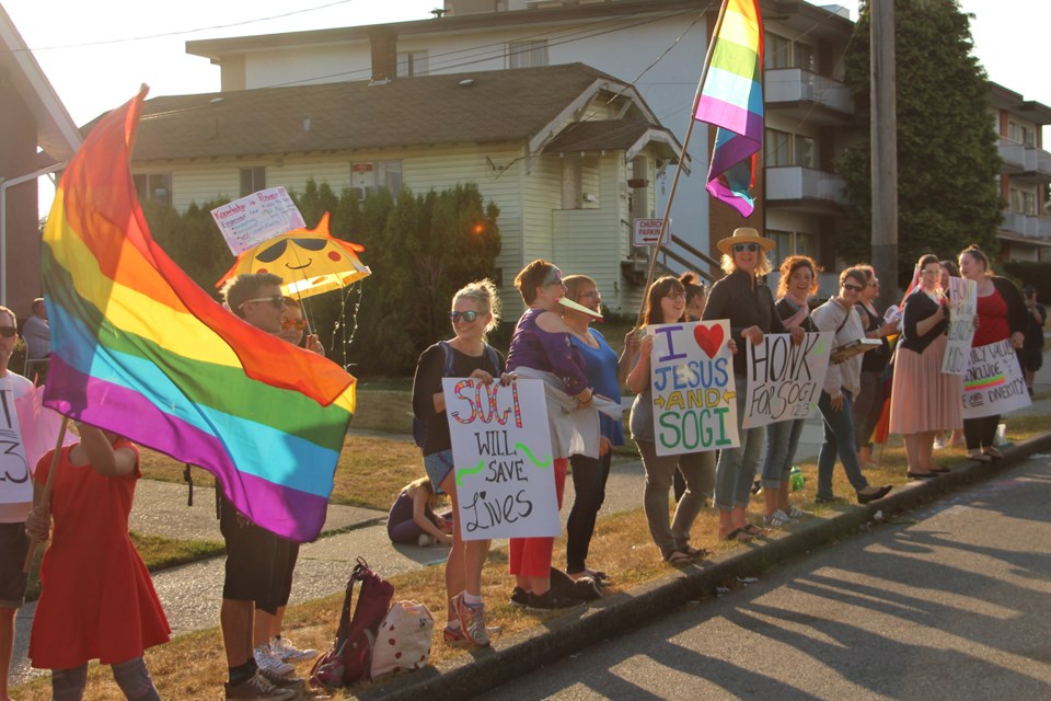 Demonstrators waved flags, signs, and cheered as cars drove by at a "love rally" outside a New West church that was hosting an anti-SOGI event Thursday evening.