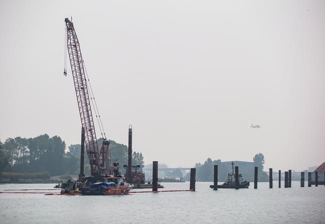 Spill response workers on boats and a crane on a barge are seen after a tugboat capsized and sank on the Fraser River between Vancouver and Richmond, B.C., on Tuesday August 14, 2018. Canadian Coast Guard spokesman Dan Bate said it's unknown what caused the George H. Ledcor tug to capsize early Tuesday near Vancouver International Airport. Four people aboard the vessel were all rescued. THE CANADIAN PRESS/Darryl Dyck