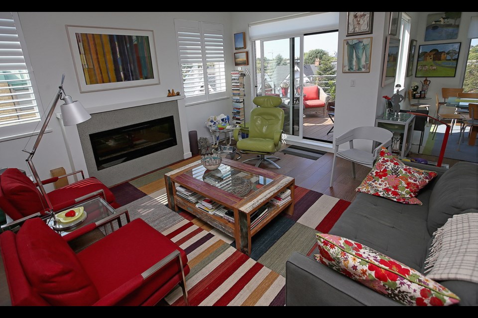 The owners' Beacon Hill Park condo is cheery and full of art and colour. A bright carpet from Gabriel Ross adds to the artistic ambience along with red armchairs from Vancouver, a celery-coloured easy chair from Florida, colourful cushions and original art. The owners added louvers on the fireplace wall window to block a view of the neighbouring building.