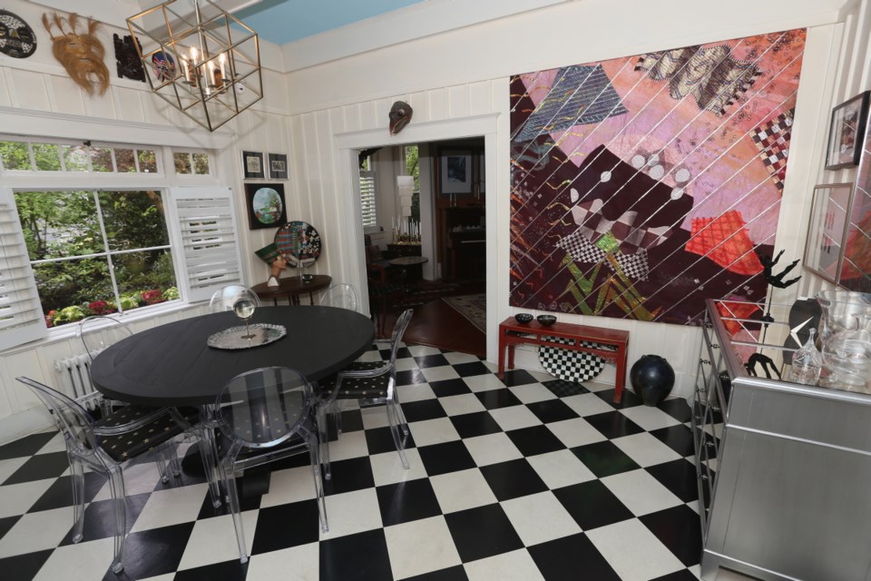 The owners laid the dining room checkerboard floor four decades ago. At right is a large wall hanging by Carole Sabiston, while elsewhere are numerous spherical images to contrast with the floor. The chairs are from Monarch Furnishings and the chandelier is from McLaren Lighting.