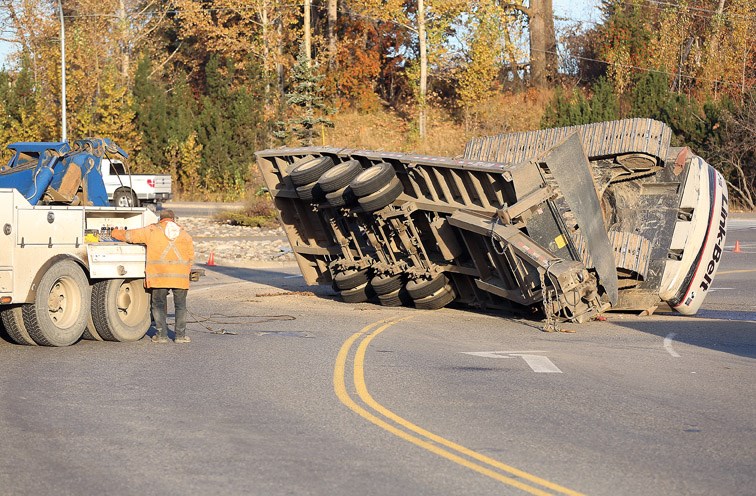 A trailer and excavator lay on its side after tipping over Friday morning on First Avenue and Carney Street.