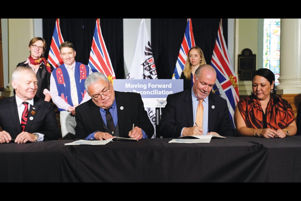 Shíshálh Nation Chief Warren Paull and Premier John Horgan sign the Foundation Agreement flanked by Scott Fraser, Minister of Indigenous Relations and Reconciliation, on the left, and shíshálh Nation Coun. Selina August on the right. Behind them stand Claire Trevena, Minister of Transportation and Infrastructure, with Sunshine Coast-Powell River MLA Nicholas Simons and Jasmine Paul, stewardship and territorial land management division manager for shíshálh Nation.