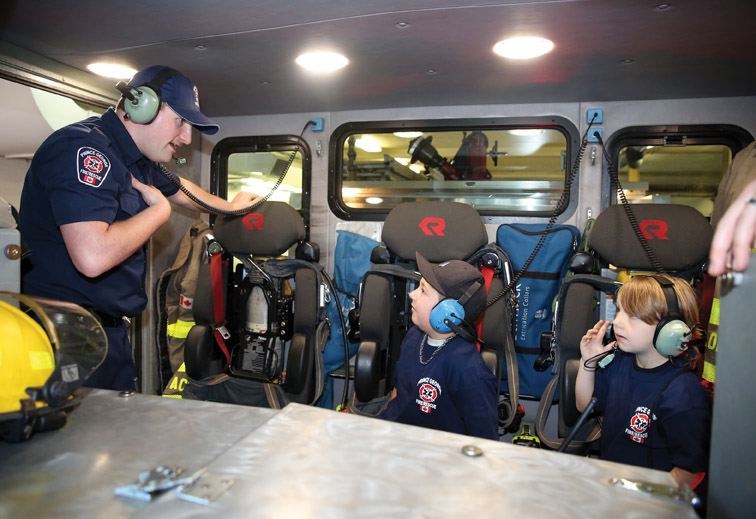 Firefighter Chris Schloegl shows off features of the jumpseats in Engine 11 to Murray Wanner, 8 from Glenview Elementary school, and Vivian Ingraham, 6, from Harwin Elementary school on Saturday morning at Prince George Fire Hall No. 1 during the annual Fire Chief for a Day event.