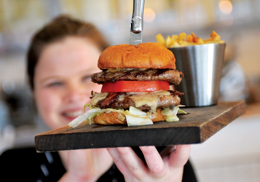 Manager Ali Millerd holds up a Boss Burger (two 65-day dry-aged beef patties, bacon and aged cheddar) at Two Rivers Specialty Meats butcher shop and eatery.