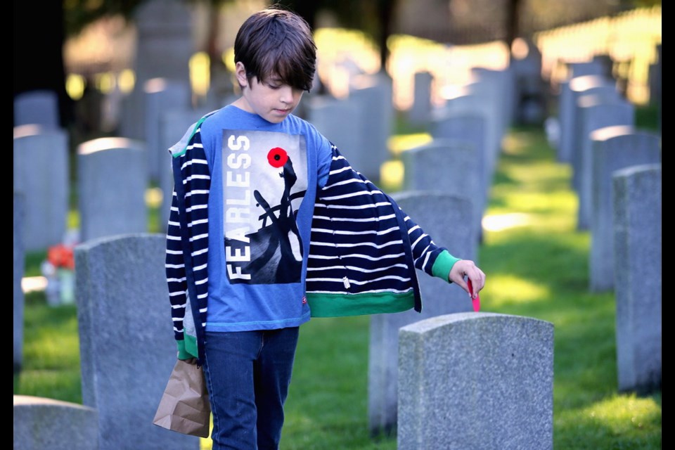 Alex Bourbeau, 11, places a poppy on a headstone at God's Acre Veterans Cemetery in Esquimalt on Friday, Nov. 2, 2018.