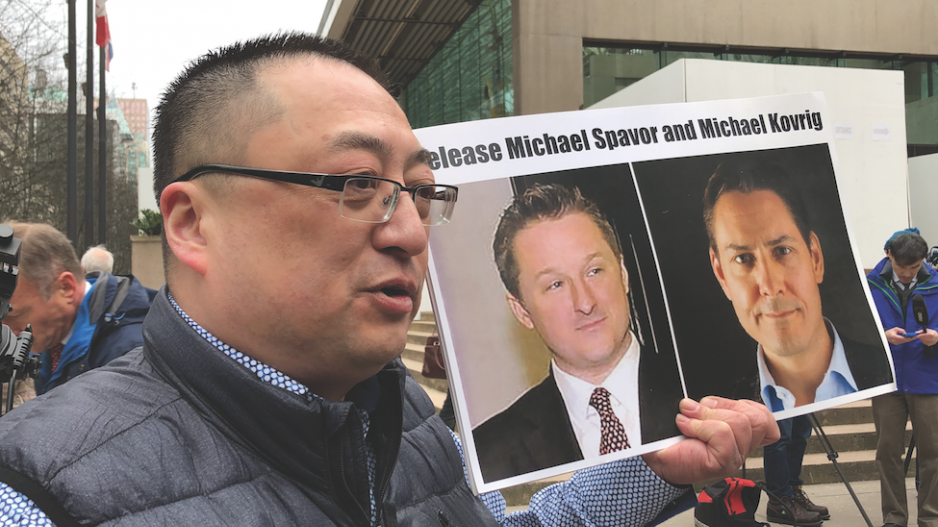 Protester Louis Huang holds photos of Michael Kovrig and Michael Spavor outside BC Supreme Court in