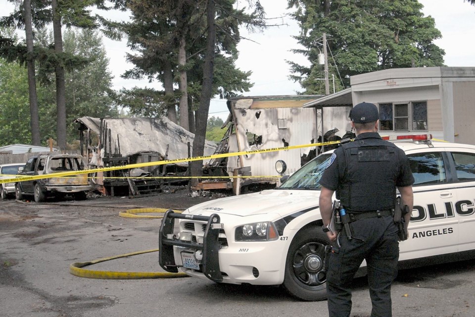 Port Angeles police Officer T.J. Mueller looks over the scene of a fire that destroyed two mobile homes at the Welcome Inn Trailer & RV Park. A woman and her three children who lived in one of the mobile homes are missing.