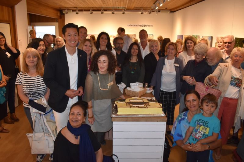 Artists, gallery staff and volunteers and attendees gather around the custom cake created by Meinhardt’s for the Ferry Building Gallery’s celebration on July 2.