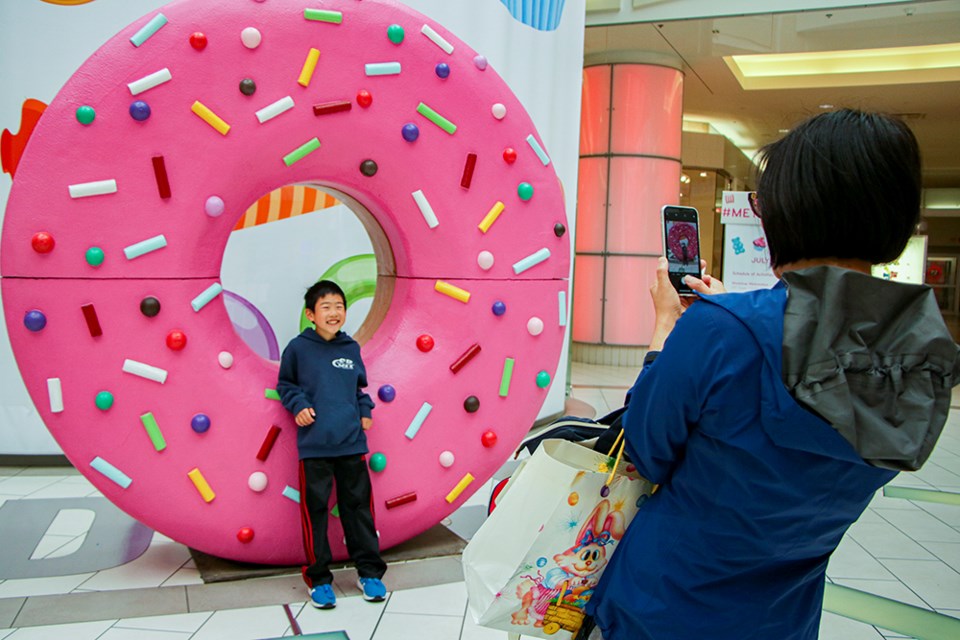 Jeffrey Young's mother takes a photo of him leaning against a giant, roughly seven-foot donut in the Snack 'N Snap display in Metropolis at Metrotown