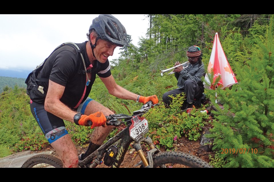 Riders ascending Frogger Trail in Stage 5 of the BC Bike Race, Earls Cove to Sechelt, were encouraged by trumpet player Randeesh and photographer Jan Brinton, who greeted every rider in the race.
