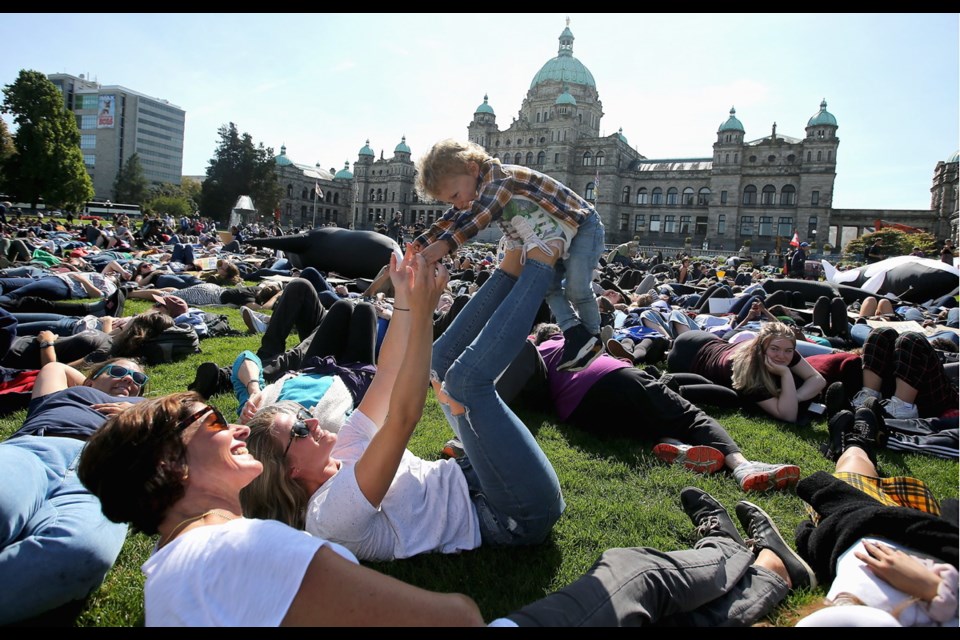 Emily Edwards, front, shares a moment with Emilyn Golden who lifts her son, two-year-old Mason, during a die-In for climate action on the legislature lawn on Friday.