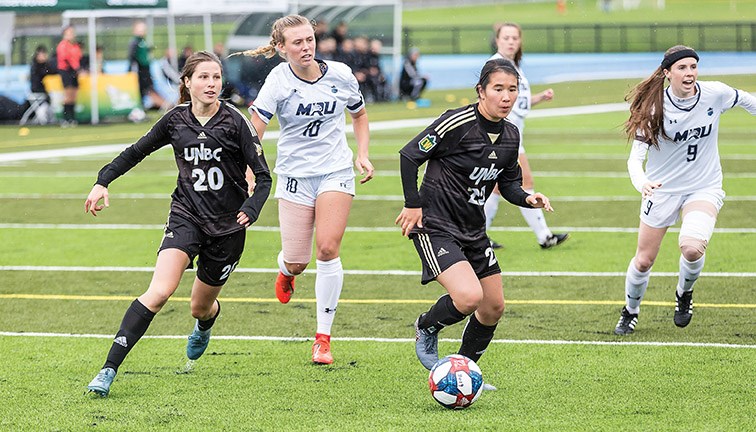 UNBC Timberwolves ball carrier Jenna Wild leads a rush with Sofia Jones (20) as she dribbles the ball ahead of the Mount Royal University Cougars Emily Wiltshire (10) and Quinn Hardstaff (9) Sunday afternoon at Masich Place Stadium. The teams played to a scoreless draw.