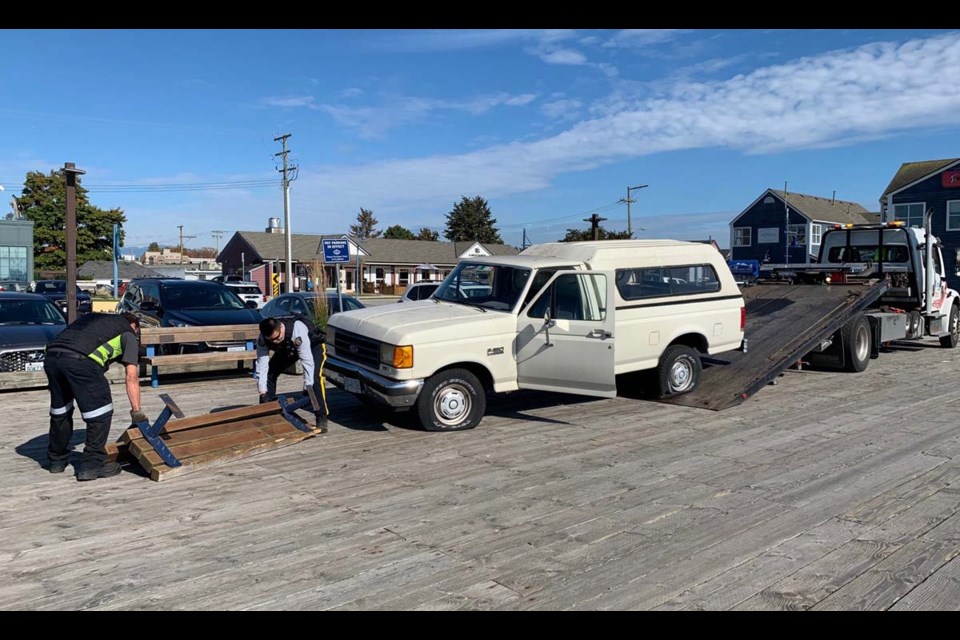 A Richmond Mountie assists a tow truck driver in lifting up the bench apparently damaged by the pick-up truck. Photo submitted