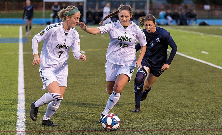 UNBC Timberwolves defender Ashley Volk, centre, passes the ball to teammate Paige Payne against Trinity Western University Spartans midfielder Gabrielle Short on Friday evening at Masich Place Stadium. Citizen Photo by James Doyle