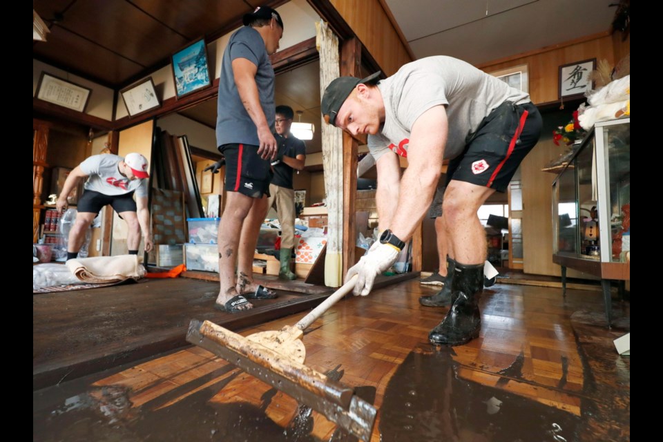 In this Oct. 13, 2019, photo, Canadian player Peter Nelson, right, volunteers to clean up mud in a house in Kamaishi, Iwate prefecture, Japan, following the cancellation of their Rugby World Cup Pool B match against Namibia due to Typhoon Hagibis. (Kyodo News via AP)
