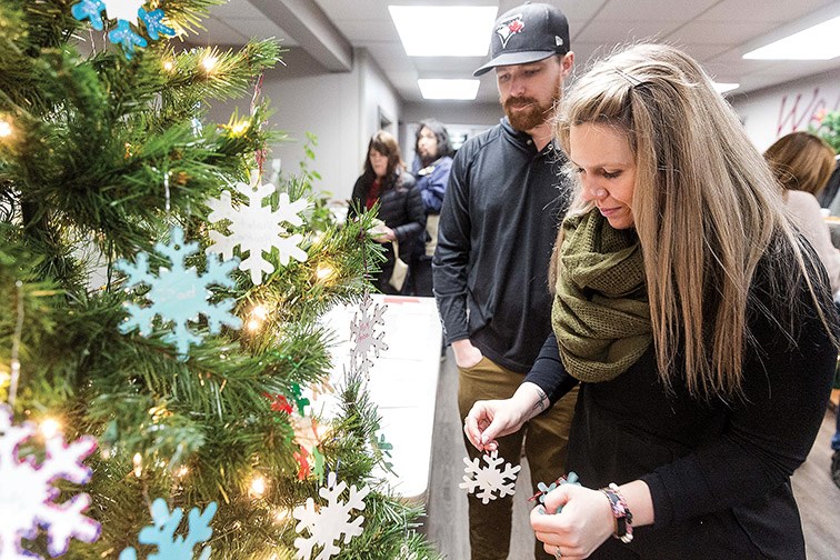 Citizen Photo by James Doyle. Kayla Anderson and her husband Kevin place handmade snowflake ornaments on a tree at Salvation Army Church on Tuesday evening during their first annual Christmas Memorial. Each ornament represents a loved one that has passed on and Kayla had memorial ornaments for her brother, sister, and mom while Kevin had a memorial ornament for a good friend.