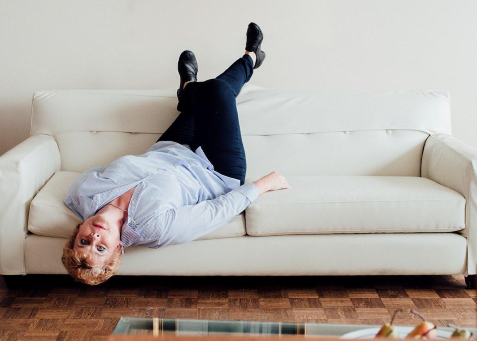 Deborah Kimmett lying feet up in the air on a tan couch.