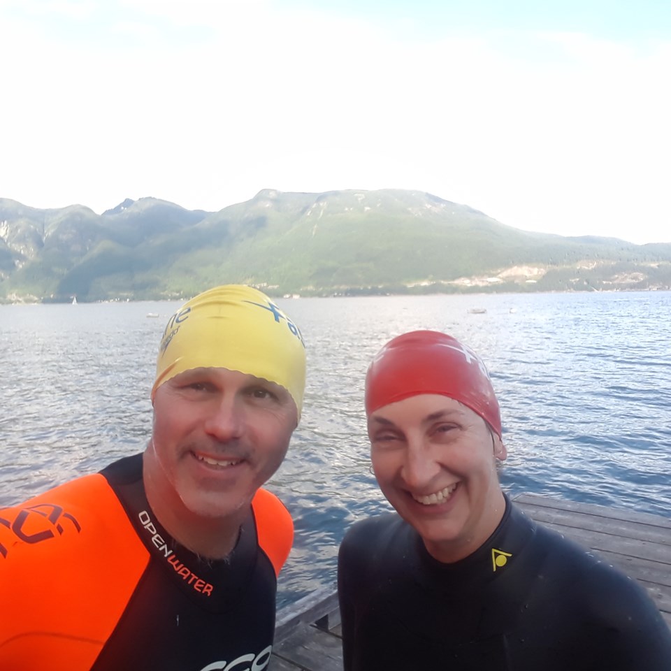 Neil and Katherine on a dock in wetsuits with the North Shore mountains behind them.