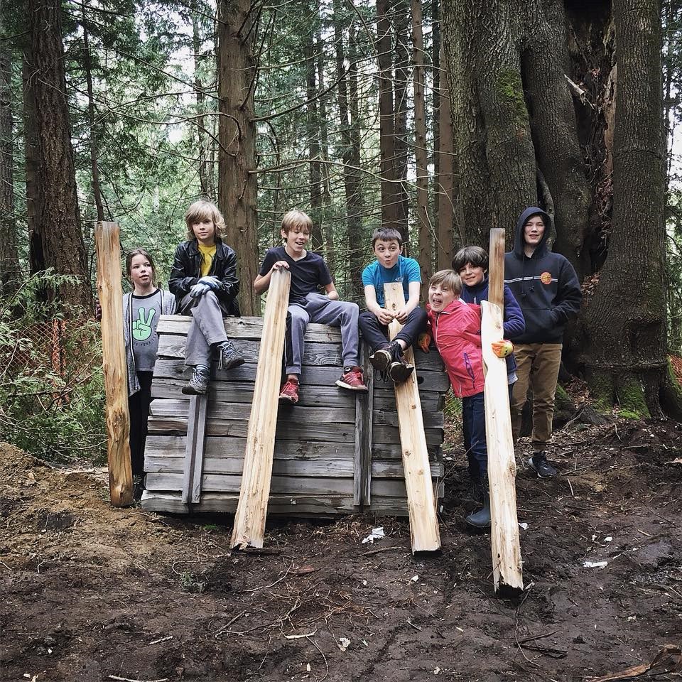 Several youth holding two-by-fours in the woods behind BICS.