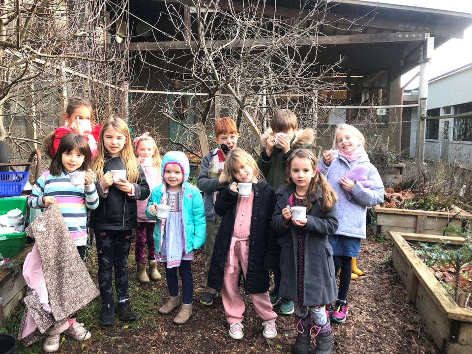Kids with tea cups in hand pose for a photo in the BICS garden
