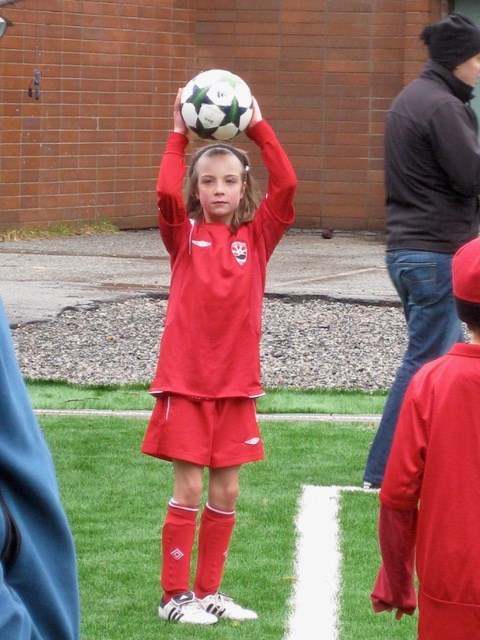 Molly as a young girl in a red jersey and shorts doing a throw-in.