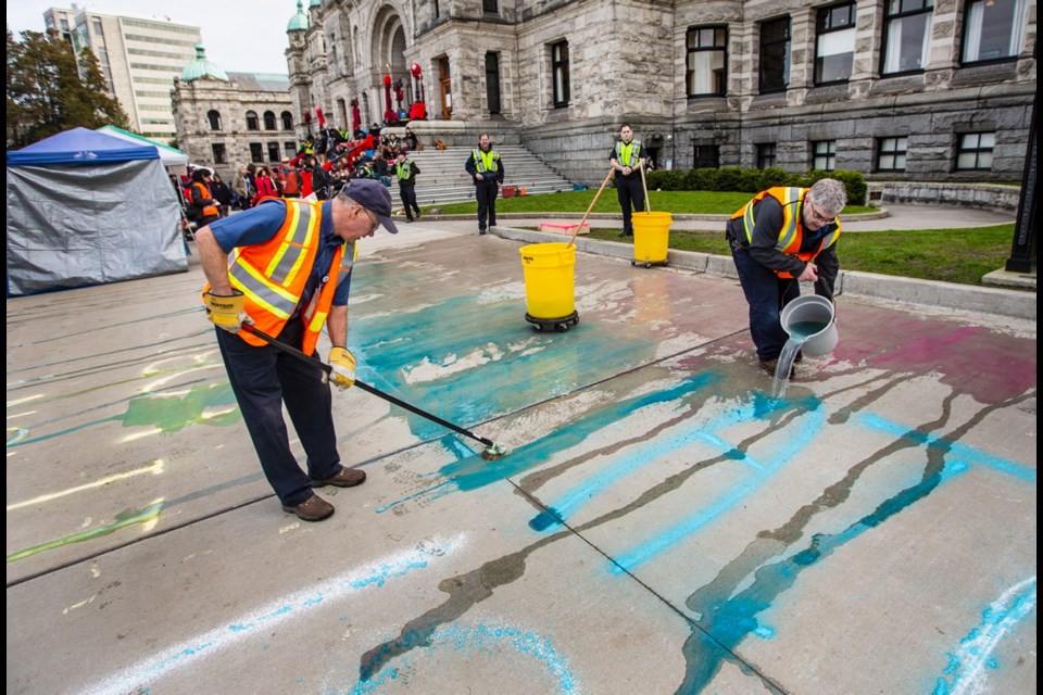 Workers clean Wet'suwet'en supporter chalk graffiti in front of the B.C. on Thursday.
