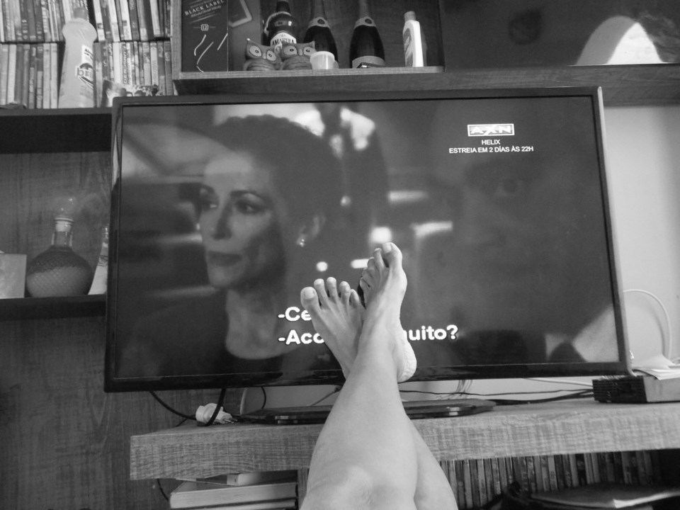 Black and white photo of feet propped up on table with TV in background