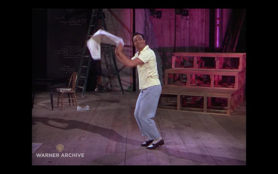 A man dancing on a soundstage with a newspaper in his hand