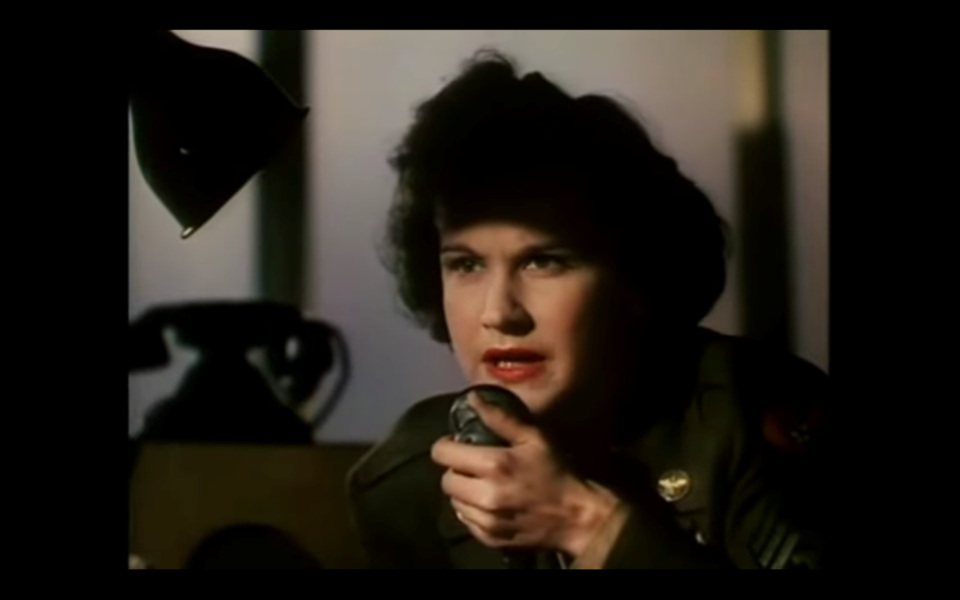 Film still of a woman in an army uniform holding a 1940s radio