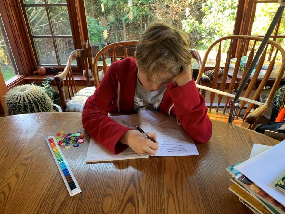 A boy sitting at a kitchen table working on schoolwork