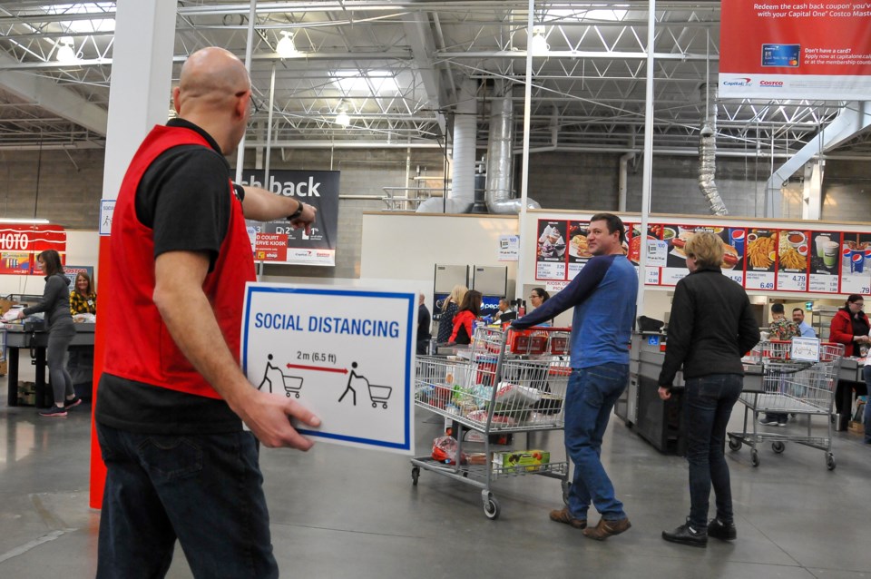 A Costco employee directs customers to ensure a level of social distancing at the check out.