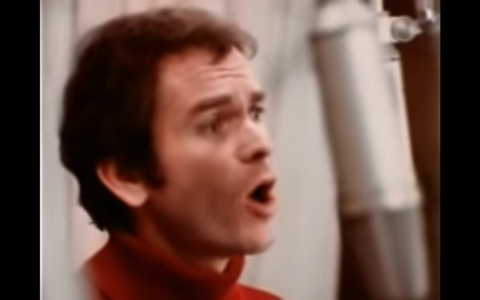 Man in a red turtleneck singing into a mic