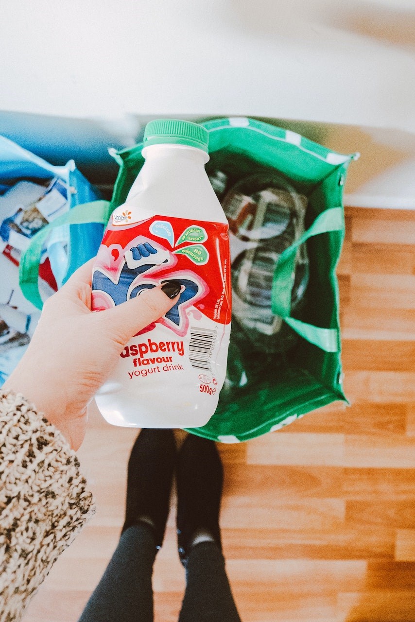 Hand holding an empty plastic drink bottle above a bag of recycling