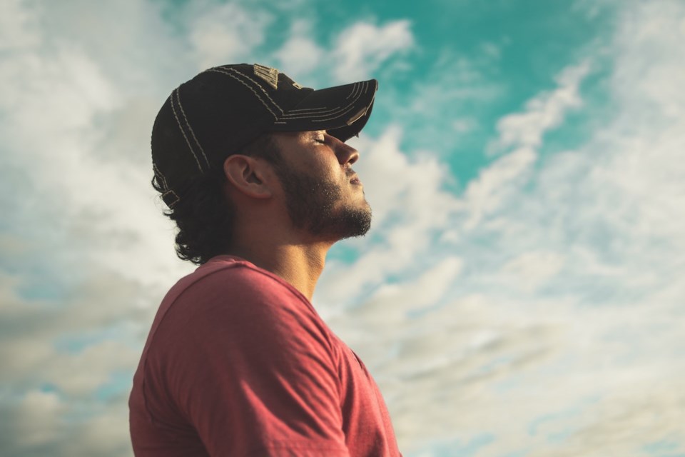 Man with black ball cap and eyes closed against a semi-overcast sky