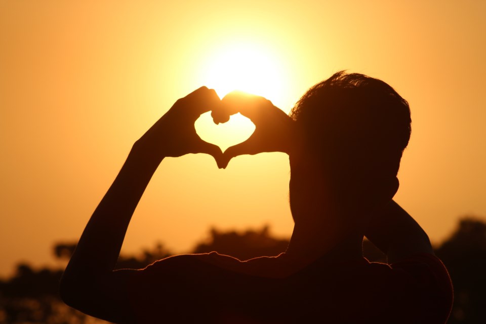 Silhouette of person holding heart to the sun