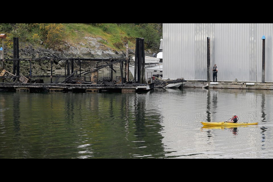 A kayaker paddles past the burnt-out fuel dock at the North Saanich Marina on Monday as crews worked to raise the boat sunk in the fire.