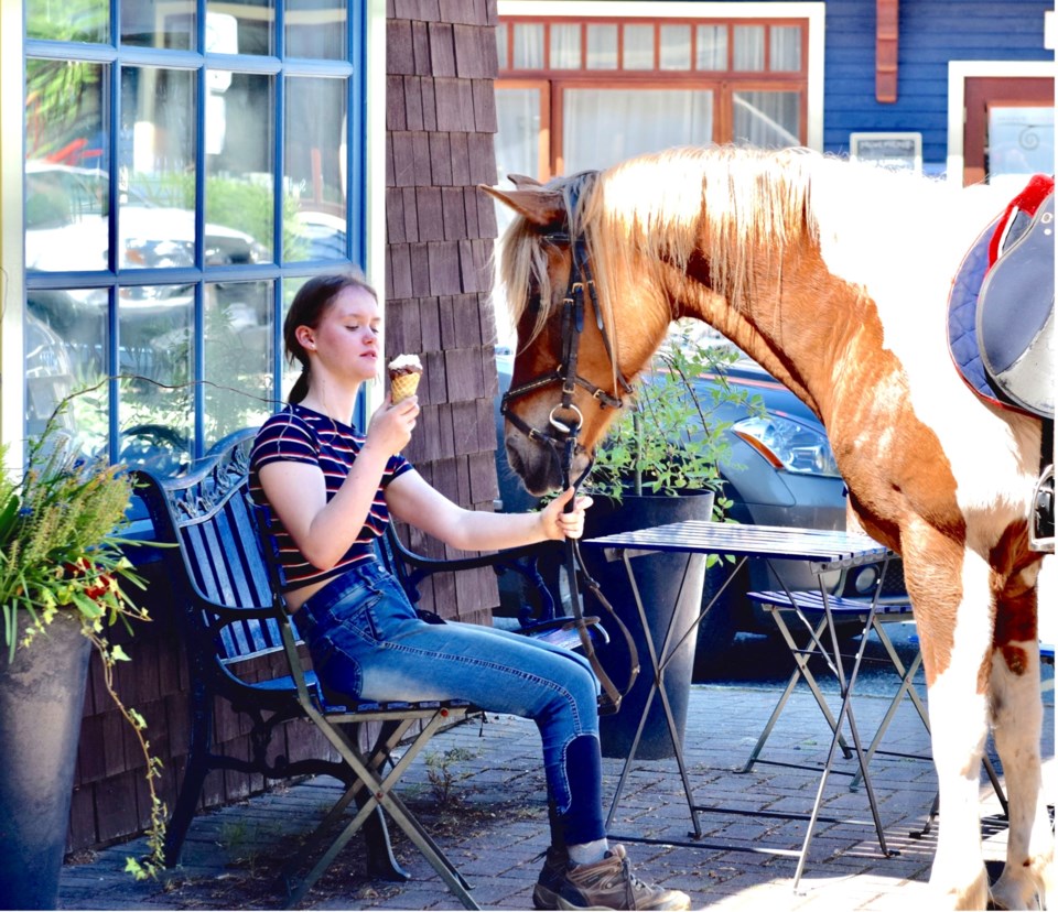 A girl eating ice cream while holding the reins of a horse