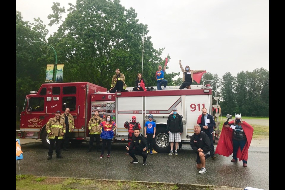 Everyday Superheroes organizers Aruna Khan and Gloria Cooper are joined by the Burnaby fiirefighters, MP Peter Julian, MLA Katrina Chen, Mayor Mike Hurley, president of the Burnaby Firefighters Association Jeff T. Clark, volunteers and more, as they all do their “superhero” pose at the drive-by food bank event held May 30.