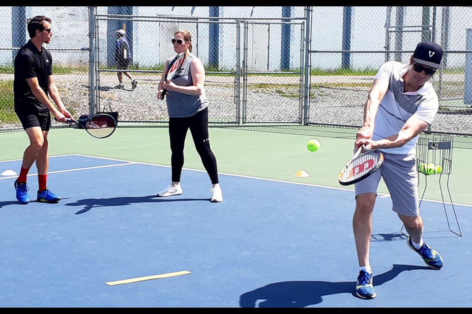 Tassi Halka hits a two-handed backhander while his wife Anna receives tips from PGTPC teaching pro Cory Fleck during their lesson. The court facility has been open since some COVID-19 restrictions were lifted on June 1st.