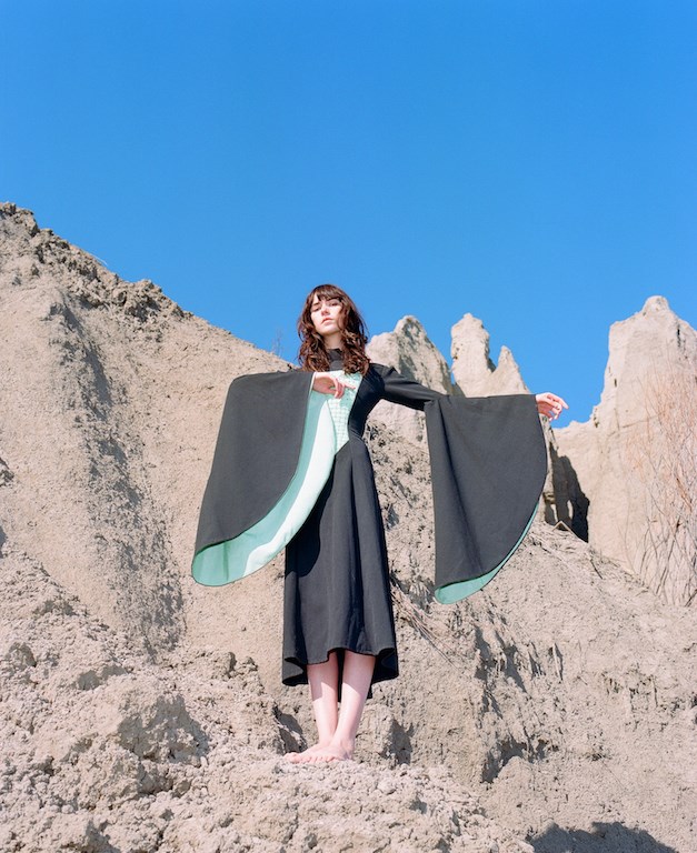 Le Ren standing on an outcrop on a cliff face wearing a black dress with green lining