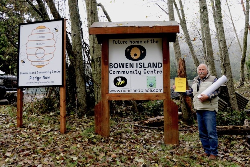 Gary Ander in front of a sign holding a laminated piece of paper